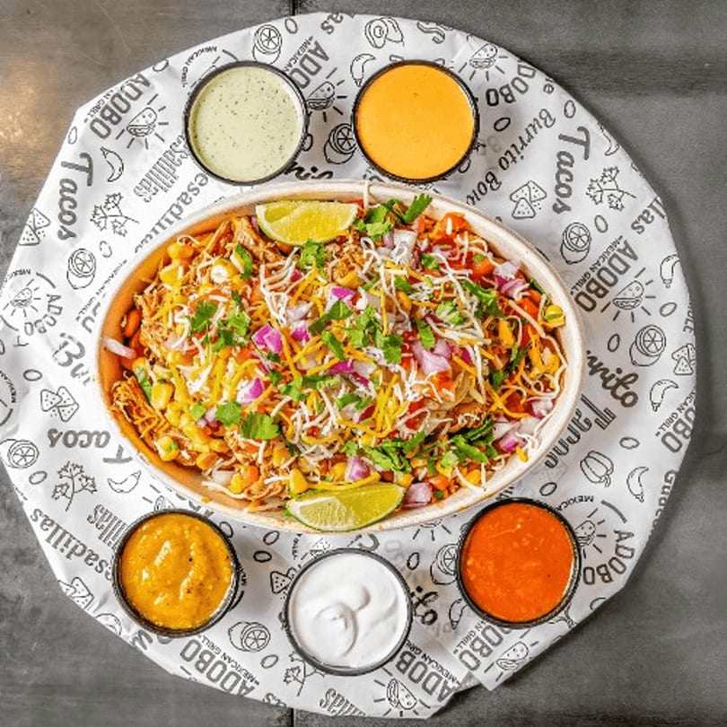 Overhead view of a colorful burrito bowl with five dipping sauces on a branded paper liner.